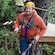 A man outfitted in a helmet and harness smiles as he walks along a suspended bridge in the tree tops
